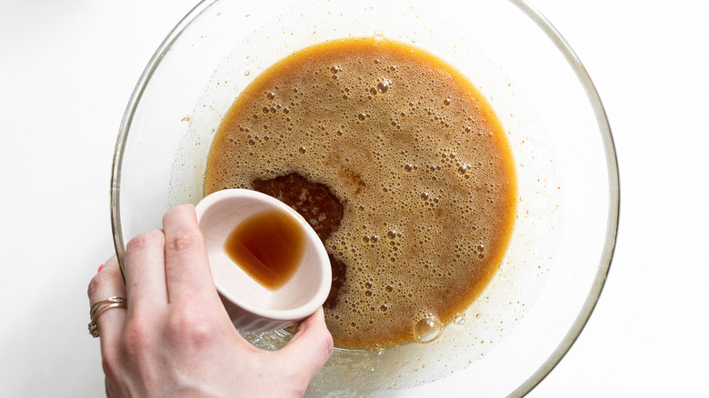 hand pouring vanilla into bowl