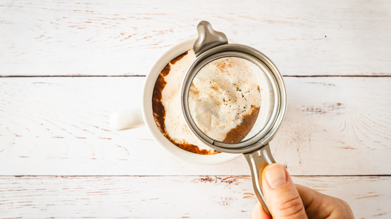 Hand holding sifter with cinnamon over cup of hot chocolate