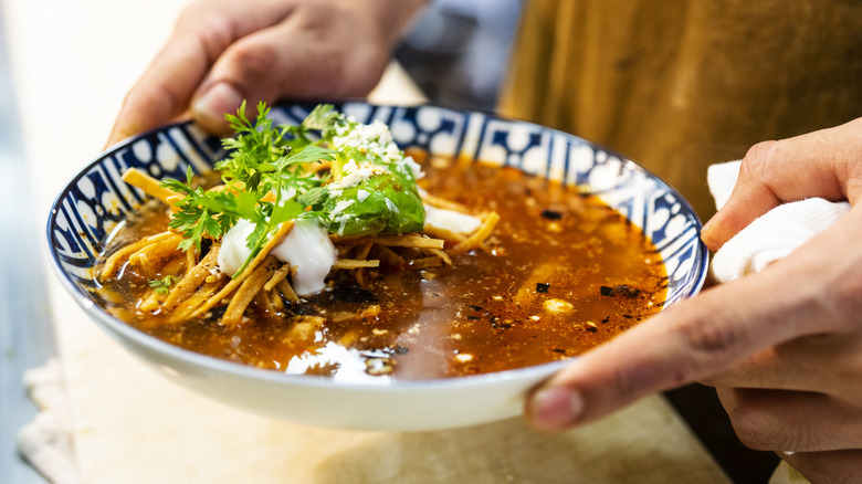 Hands holding a bowl of tortilla soup