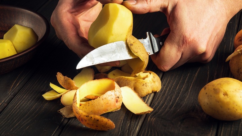 cook with knife peeling potatoes