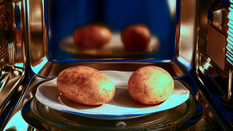 two baked potatoes on a plate inside a microwave