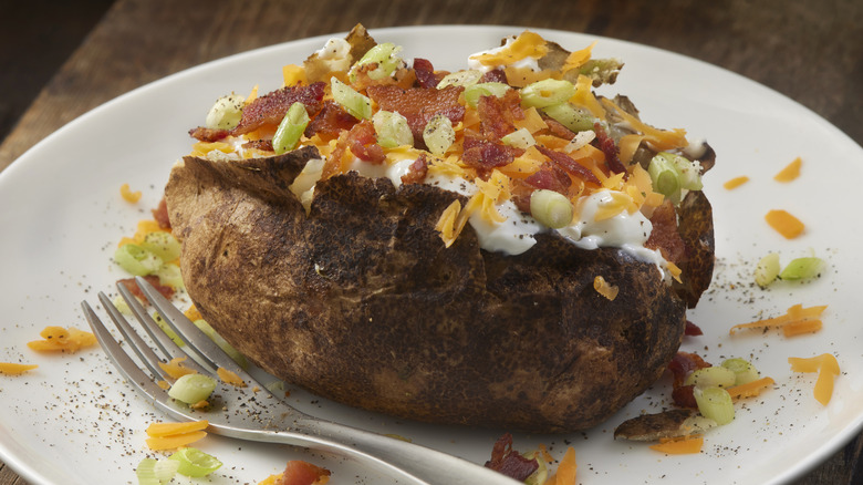 loaded baked potato with sour cream, cheese, chives, and  bacon on a white plate