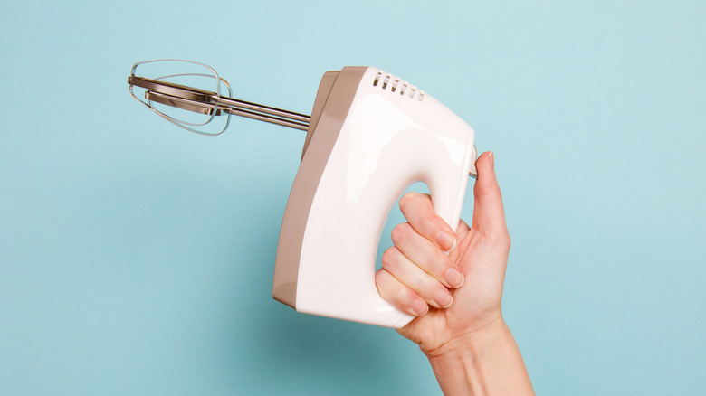 Hand holding an electric mixer on blue background