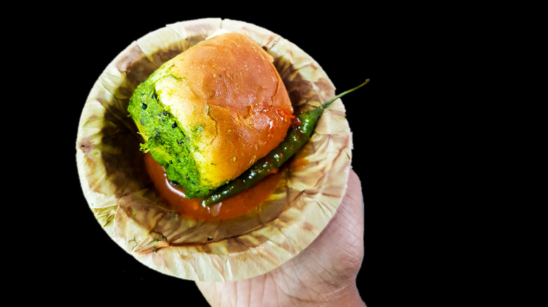 Hand serving a vada pav sandwich 