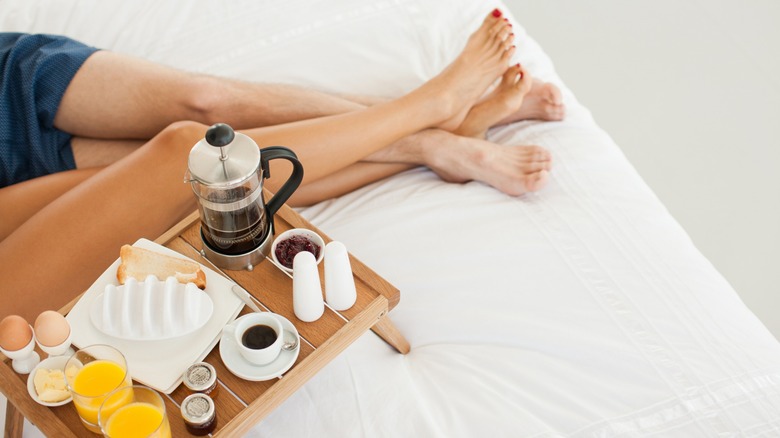 The legs and breakfast tray of a couple eating breakfast in bed