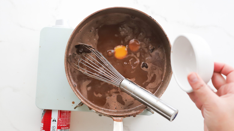 Adding yolks to saucepan of chocolate pudding with whisk