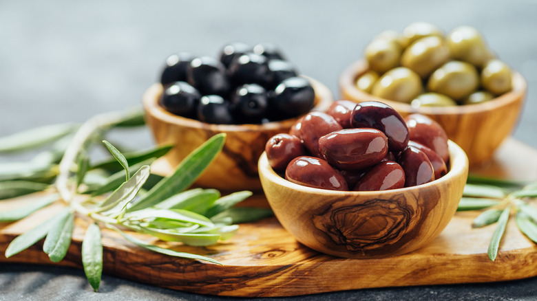 three wooden bowls of olives and olive branch on board