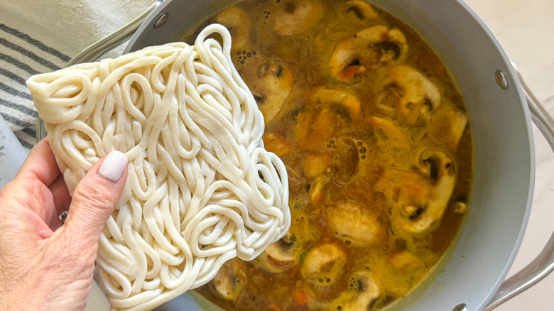 hand adding noodles to pot