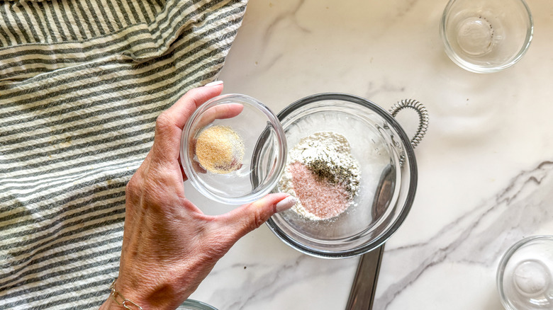 Hand adding garlic granules to a bowl of dry ingredients