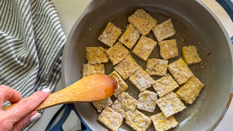 Stirring tempeh in pan with a wooden spoon