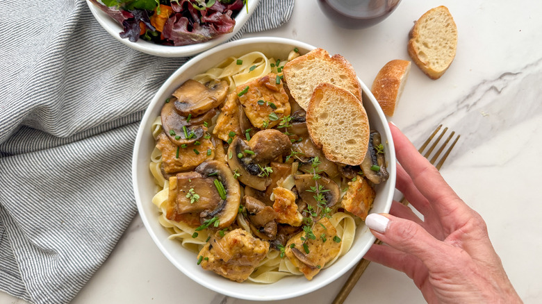 Hand putting out white bowl of tempeh Marsala