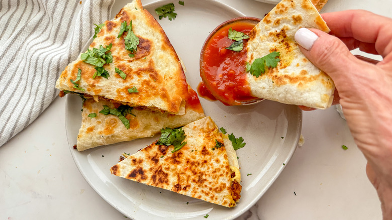 hand dipping quesadilla in salsa