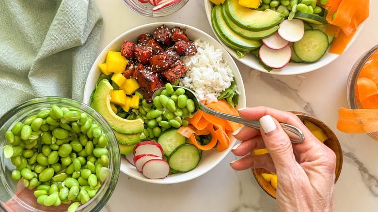 hand adding edamame to bowl