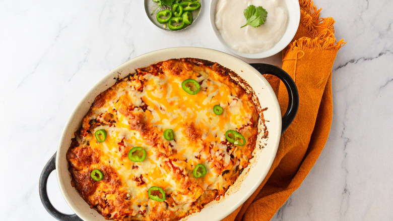 Enchiladas besides bowls of jalapeno and sour cream