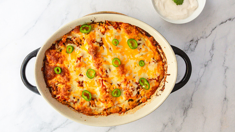 Baked enchiladas besides bowl of sour cream