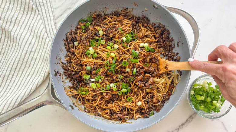 Dan dan noodles stirred in pan by wooden spoon