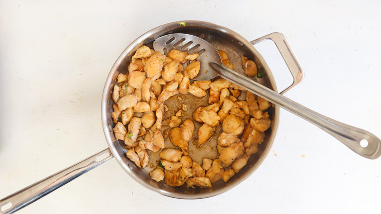 browned chicken in a pan with slotted spoon