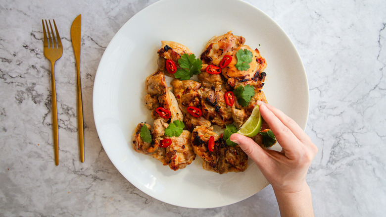 Squeezing lime onto cooked chicken on white plate