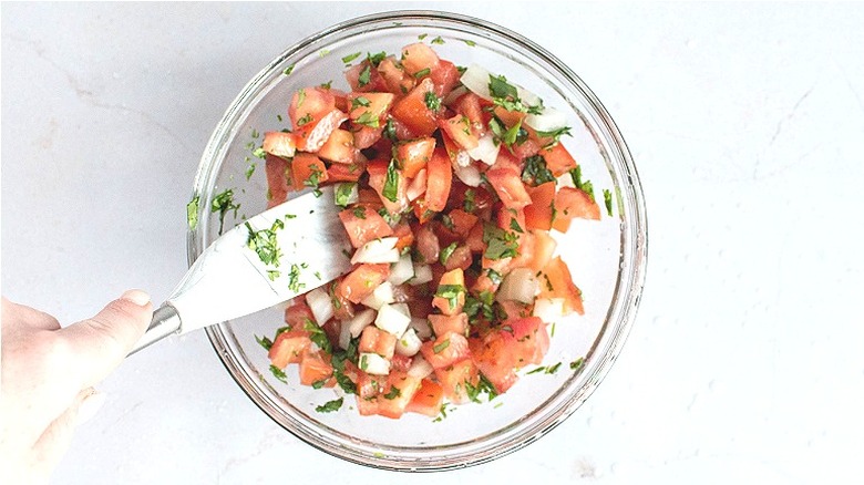 Spatula stirring bowl of tomatoes and onions