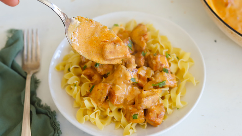 spoon ladling pork paprikash over noodles