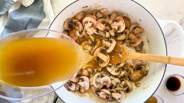 pouring broth into pot of mushrooms and onions