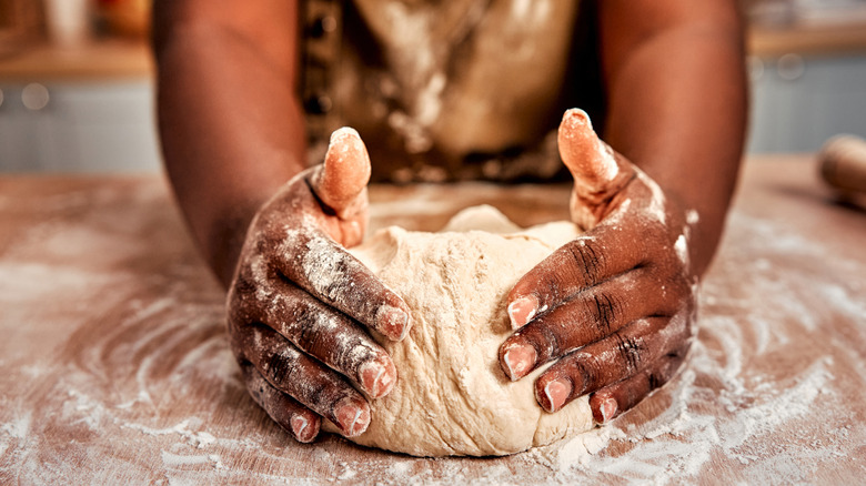 A person kneading bread dough on a floured counter