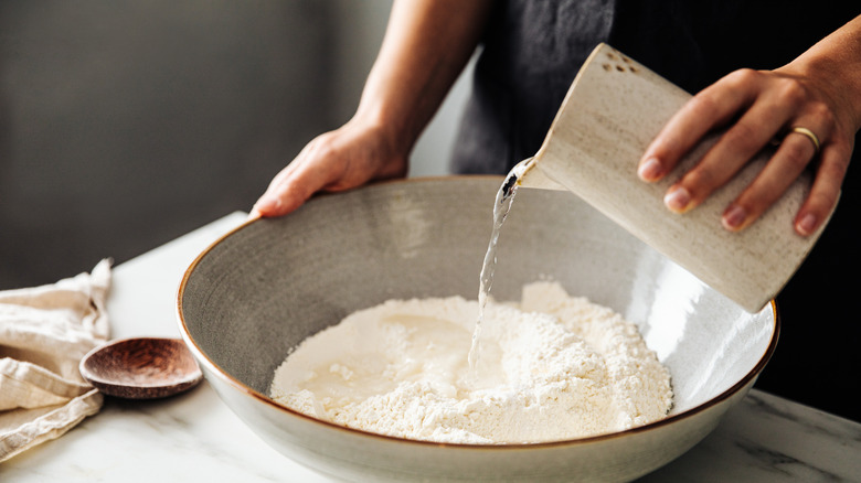 Person adding water to a large bowl of flour