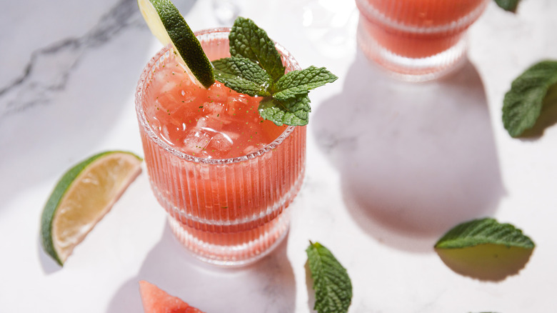 One glass with watermelon margarita mocktail, lime and mint around it