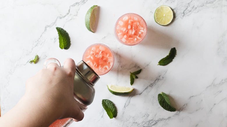 Pouring cocktail from a shaker into two glasses with watermelon margarita mocktails