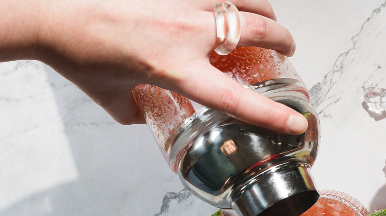 Pouring cocktail from a shaker into two glasses with watermelon margarita mocktails