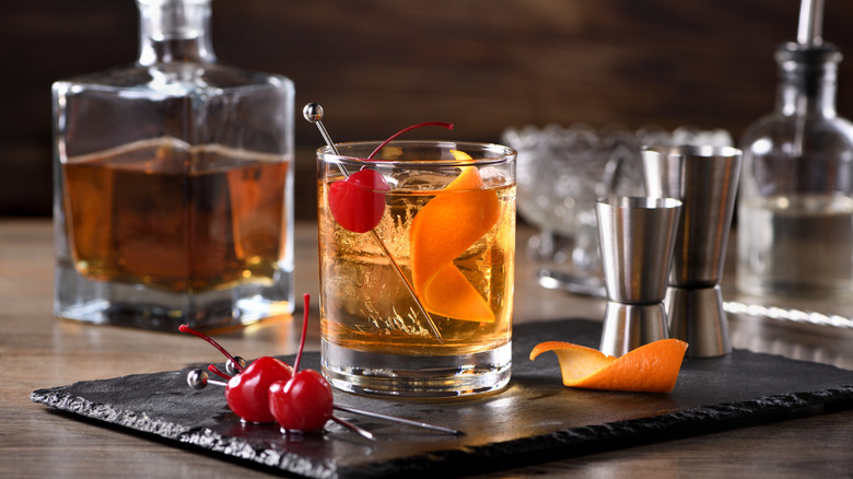 ingredients and kit for an old fashioned cocktail, pictured with cherry and orange peel