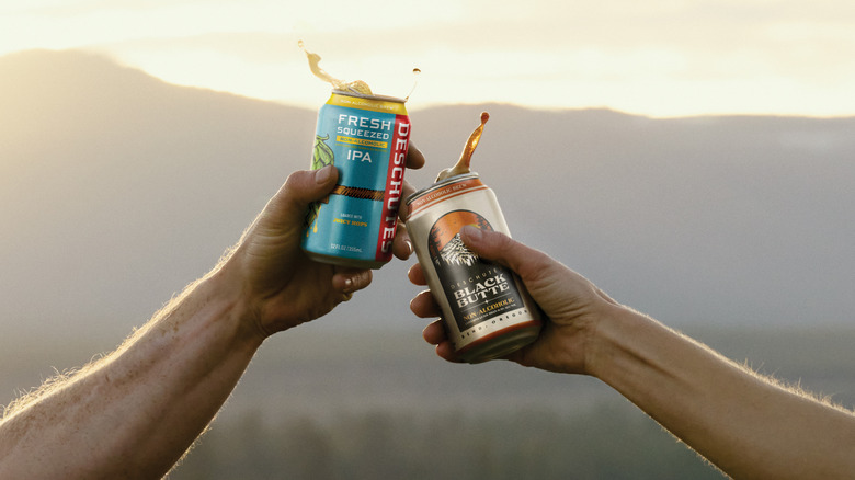 Two people using Deschutes NA beer cans to cheers