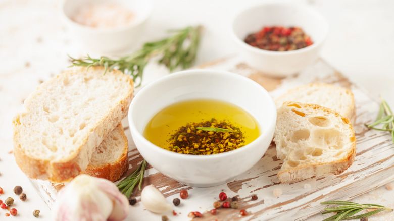 slice of bread and bowl of bread dipping oil surrounded by garlic and spices