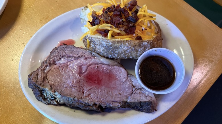 Prime rib cut with loaded baked potato and side of au jus from Texas Roadhouse.