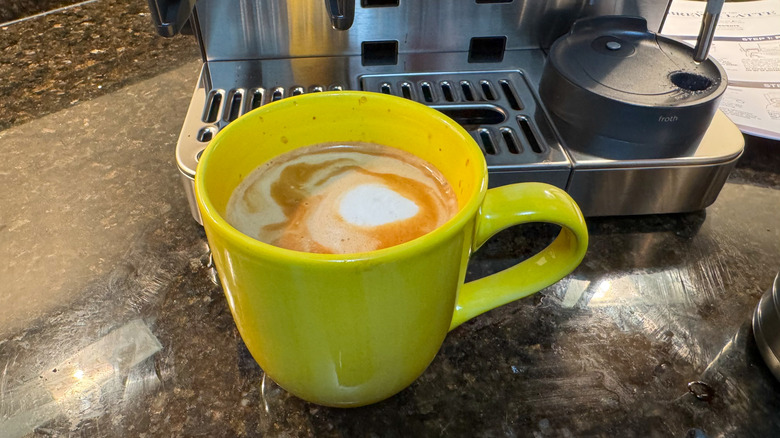 Yellow cup filled with milky coffee next to espresso machine