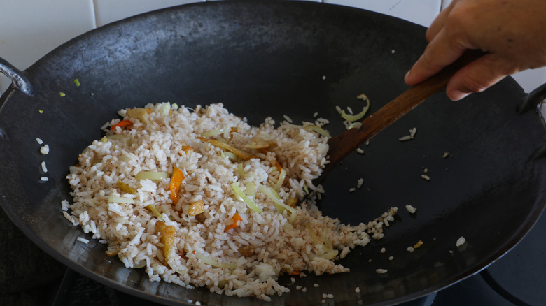 hands frying rice in wok