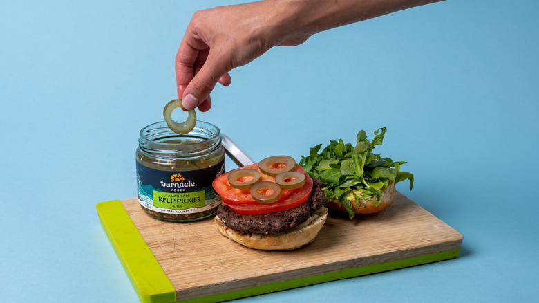 hand putting kelp pickles on burger 