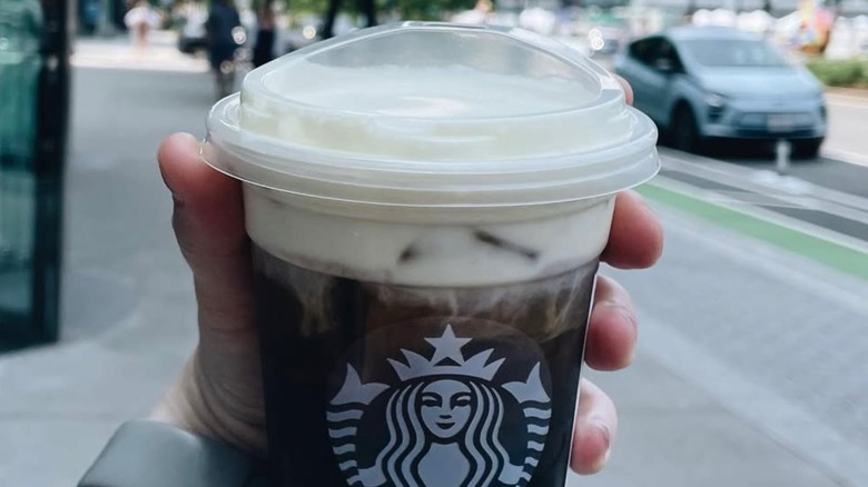 Hand holding a Starbucks Iced Coffee topped with Oleato Golden Foam