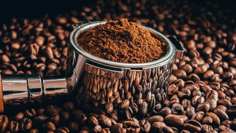 A portafilter with ground coffee resting on beans