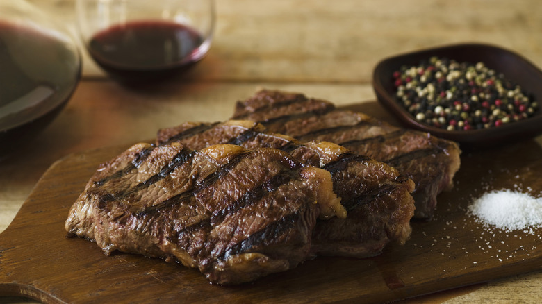 Grilled meat on wooden platter beside salt and other items
