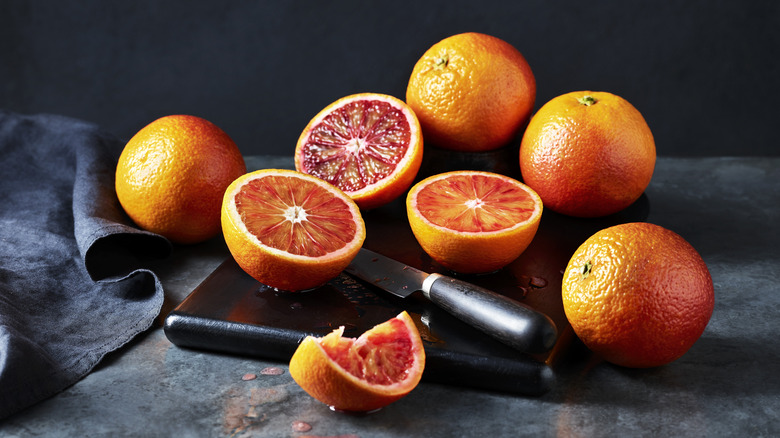 Halved and whole blood oranges on counter with knife