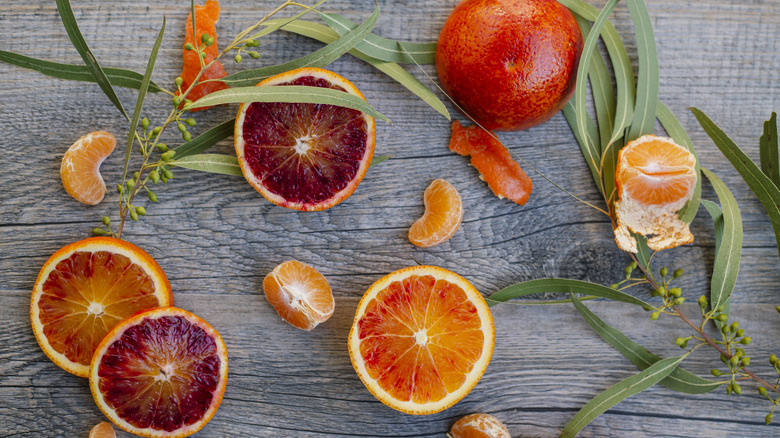 whole and sliced assorted blood oranges on a wooden surface with greens