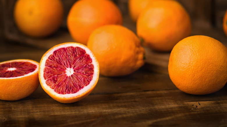 one sliced and several whole blood oranges on wooden surface