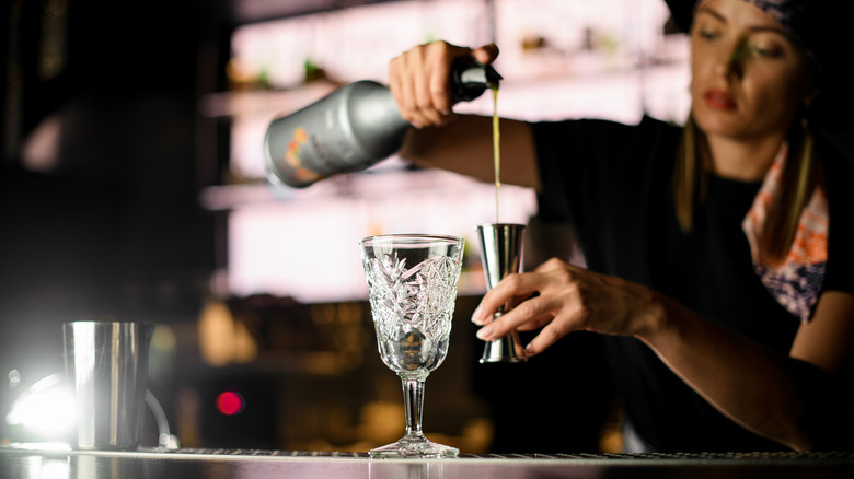 A bartender measuring alcohol for a cocktail