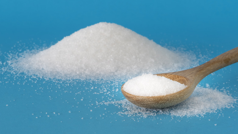 light blue background with pile of white granulated sugar and wooden spoon filled with more sugar