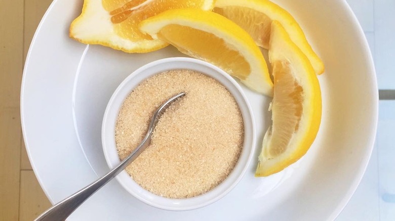 close up of white bowl of golden caster sugar and sliced lemons on white plate