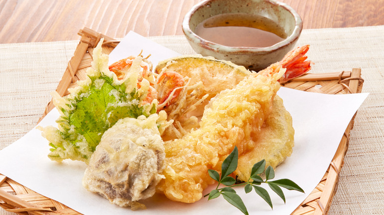 Shrimp and vegetable tempura with citrus ponzu served on a paper covered bamboo platter atop a beige mat on a light wood table