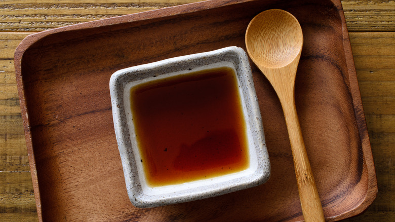 Citrus ponzu sauce in a square ceramic dish sitting on a wooden tray on a wooden table with a wooden spoon