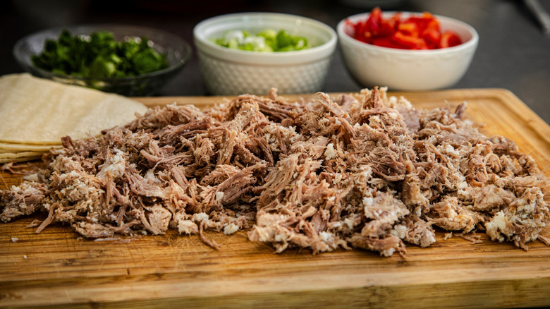 shredded carnitas on cutting board with tortillas and toppings