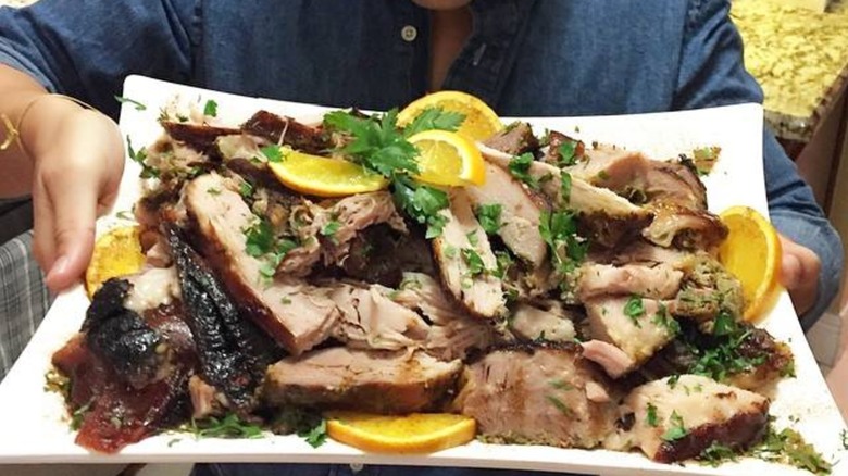 cut pernil on a platter with orange slices and herbs